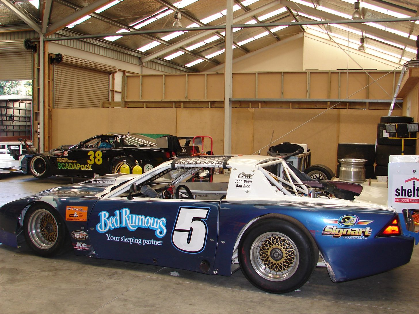 Andy Greenslade's #5 Bed Rumours Camaro in a workshop, with a #38 SCADAPack car behind