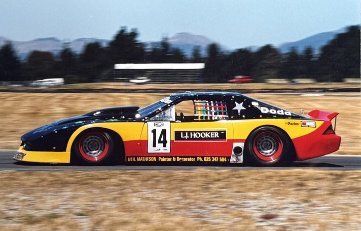 Lindsay Dodd's #14 L.J. Hooker Camaro replica at speed, hills behind