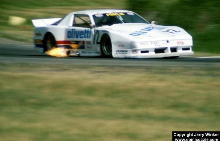 The #72 Olivetti / Rain-X Pontiac spitting flames from the exhaust on a grass-lined circuit